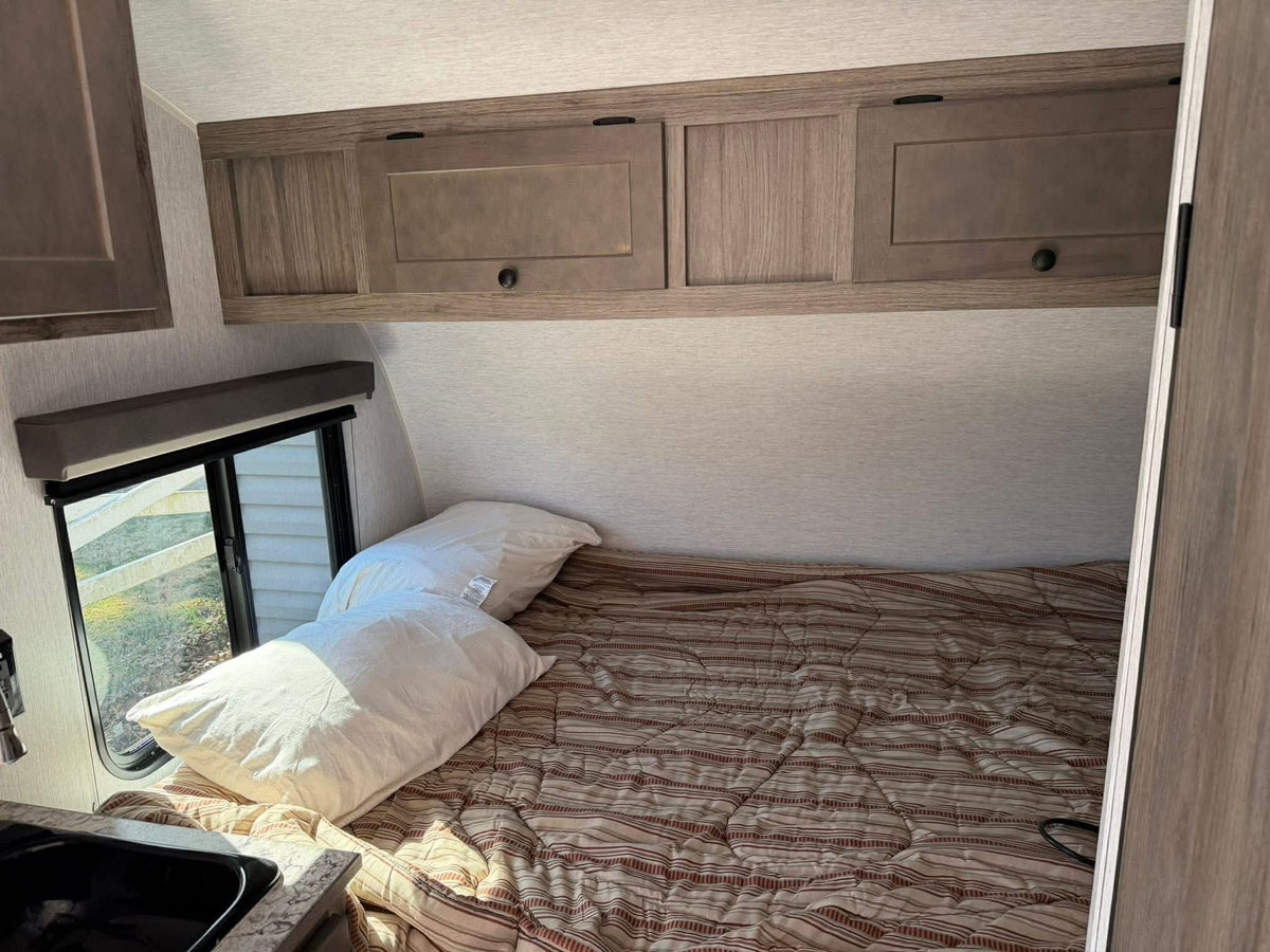 Inside an RV rental: bedroom area with a comfortable bed, wood-look cabinets, and a sunlit window for travelers. — photo 9