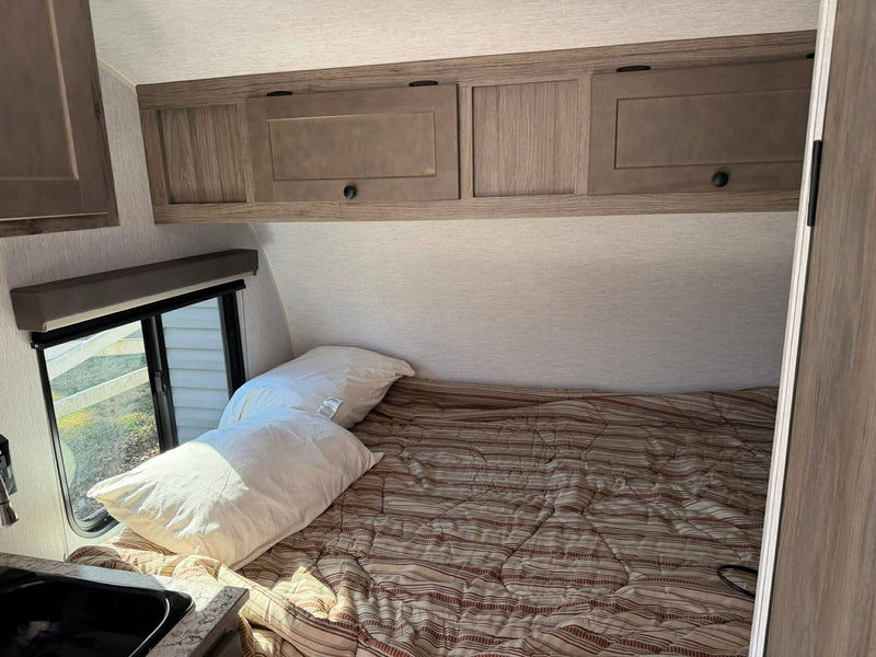 Inside an RV rental: bedroom area with a comfortable bed, wood-look cabinets, and a sunlit window for travelers. — photo 9