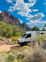 RV rental camper van parked at a scenic national park campground with majestic mountains and a bright blue sky.