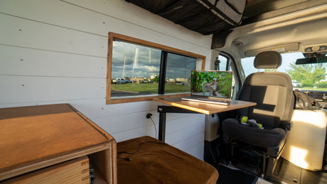Interior of an RV rental showing a laptop on a table, a window view, and comfy seating. Perfect for remote work & van life.