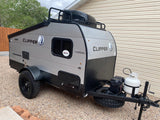 A rugged Coachmen Clipper travel trailer, ready for an rv rental adventure, with off-road tires, propane tank, and roof storage.