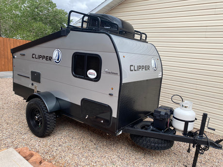 A rugged Coachmen Clipper travel trailer, ready for an rv rental adventure, with off-road tires, propane tank, and roof storage.