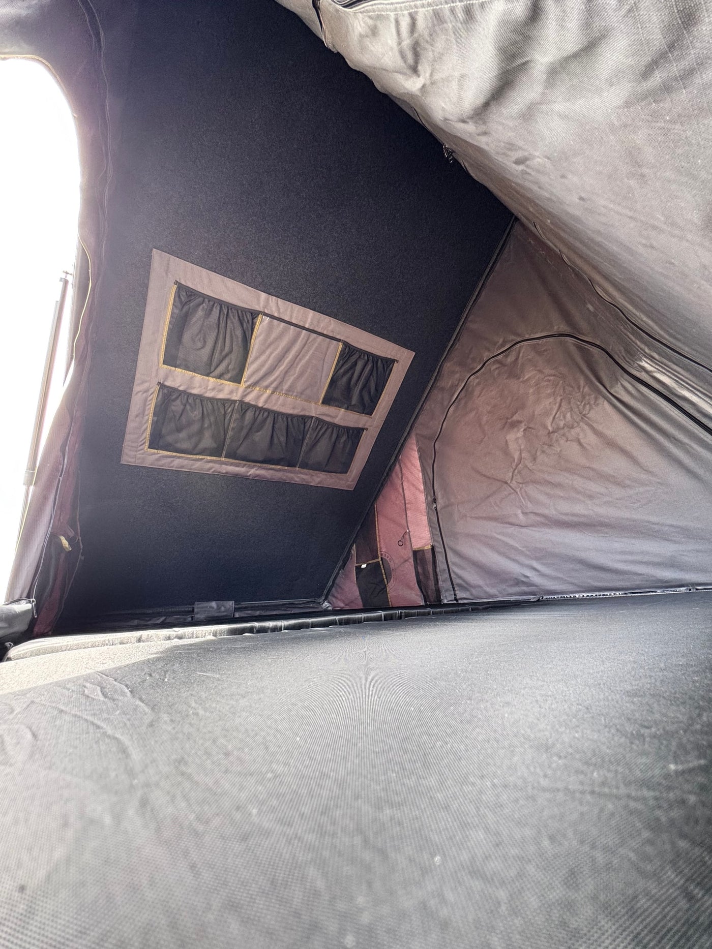 Inside a spacious RV rental rooftop tent, featuring a sleeping platform, mesh storage pockets, and natural light. — photo 8