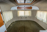 Cozy RV rental interior featuring a green bed, light curtains, overhead storage, and a skylight.