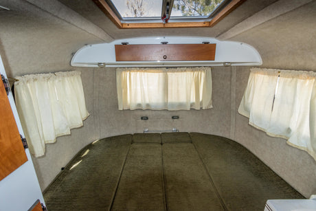 Cozy RV rental interior featuring a green bed, light curtains, overhead storage, and a skylight.