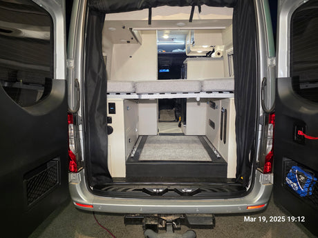 Explore the back of this RV rental camper van: a cozy interior with a raised bed, under-bed storage, and conversion amenities.