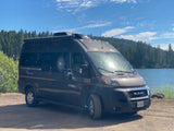RV rental camper van parked by a serene lake with a forest background. Ready for a nature adventure.