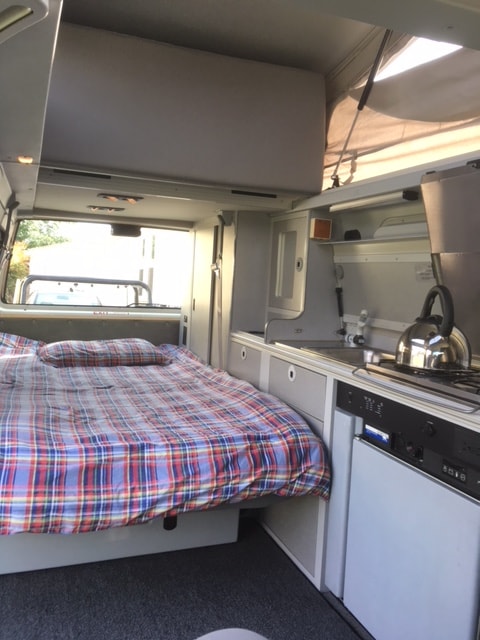  plus two dining tables set for compact travel meals.|Relax in this rv rental! Cozy plaid bed inside a pop-top camper — photo 6
