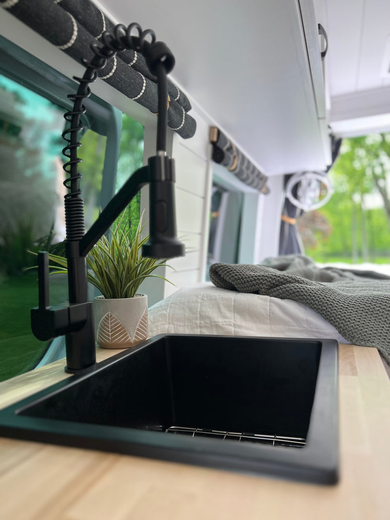 Explore the road in style! This RV rental features a modern kitchenette with black sink, faucet, wood counters, and cozy bed. — photo 14