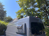 A grey camper van, an ideal rv rental, parked under trees. Its side window is open on a clear, sunny day.