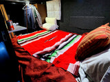 This RV rental features a cozy sleeping area with a vibrant red blanket, storage nets, and hanging clothes.