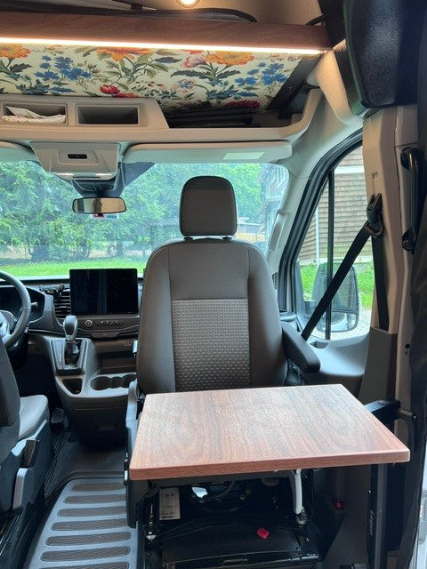 RV rental interior: passenger seat swiveled with a table, ample overhead storage, and a vibrant floral ceiling liner.