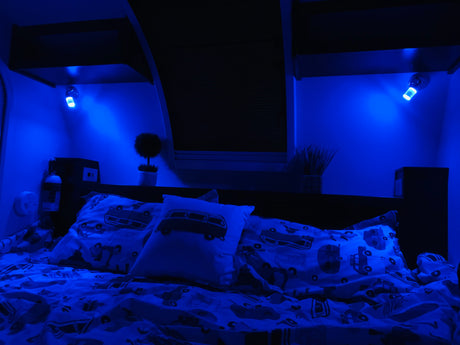 Cozy RV rental bedroom at night, featuring blue LED lighting, patterned bedding with vintage vans, and practical amenities for travel.