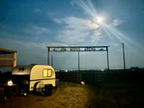 A white and dark teardrop RV rental is parked at Jim Moss Arena under a bright moonlit sky. Ideal for a rural getaway.