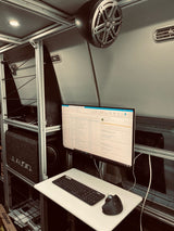 Inside an RV rental: a compact mobile office setup with a monitor, keyboard, ergonomic mouse & JL Audio system.