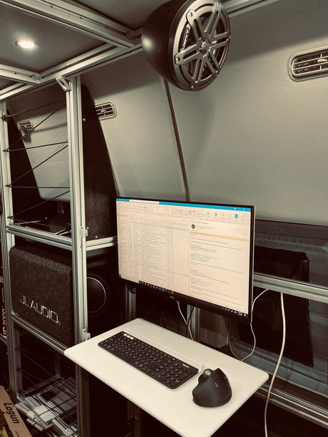 Inside an RV rental: a compact mobile office setup with a monitor, keyboard, ergonomic mouse & JL Audio system.