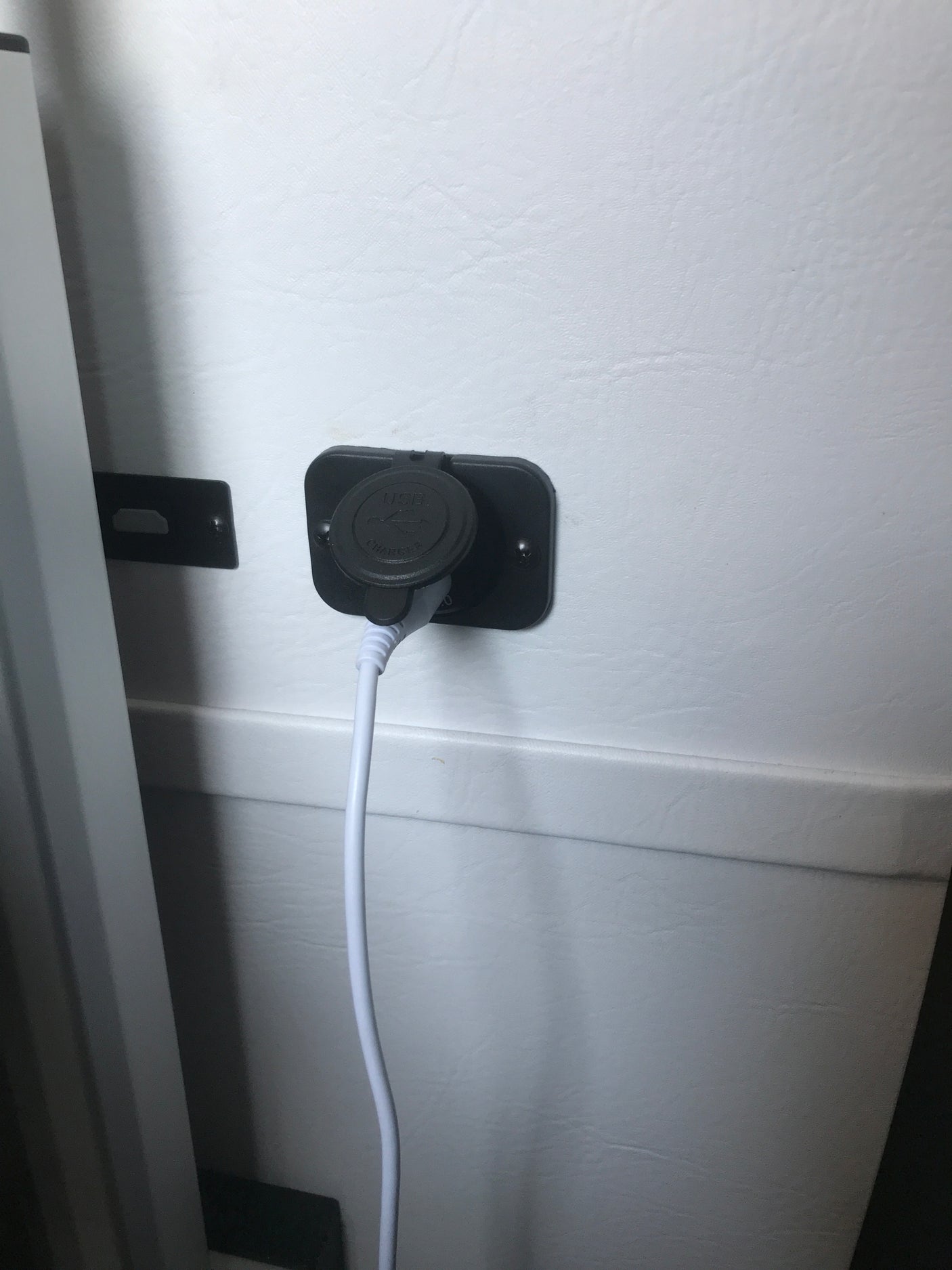 RV rental USB charger with a white cable plugged in, mounted on a light-colored interior wall for device power.