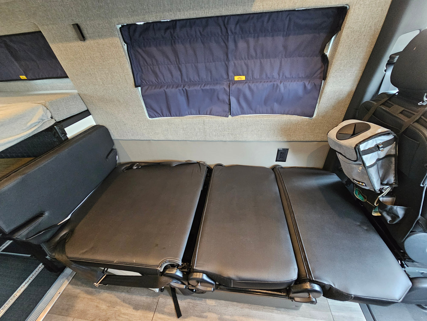 RV rental interior: black convertible seating that transforms into a bed, dark window shades, and a raised sleeping area.