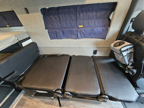 RV rental interior: black convertible seating that transforms into a bed, dark window shades, and a raised sleeping area.