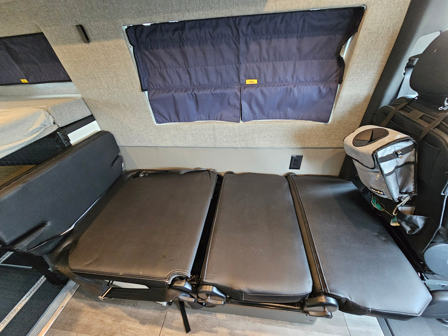 RV rental interior: black convertible seating that transforms into a bed, dark window shades, and a raised sleeping area.