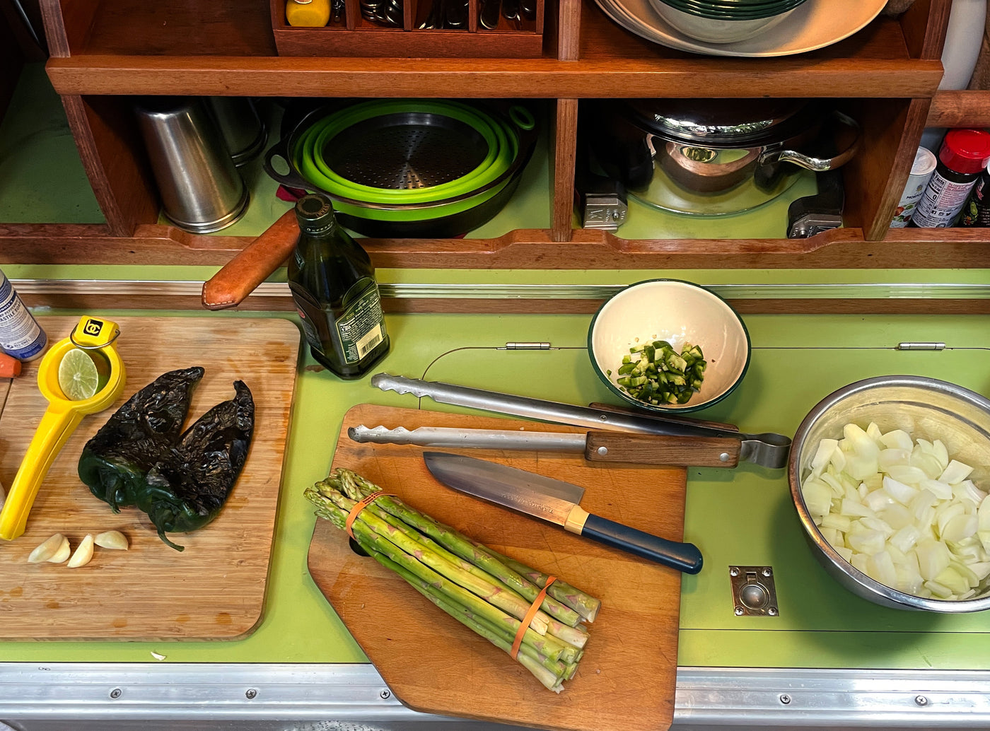 A compact RV rental kitchen boasts organized shelves and a green counter, where roasted peppers, asparagus, and chopped onions are prepped. — photo 13