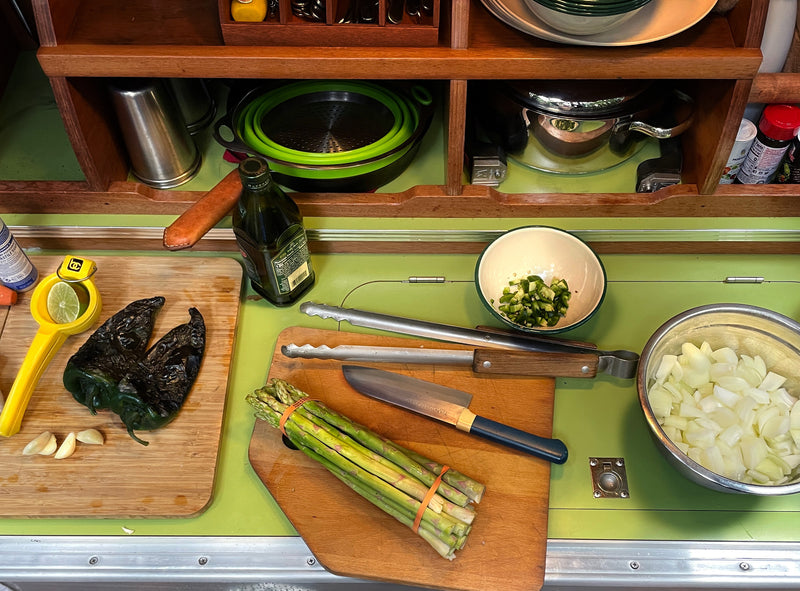 A compact RV rental kitchen boasts organized shelves and a green counter, where roasted peppers, asparagus, and chopped onions are prepped. — photo 13