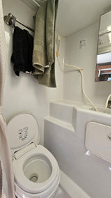 RV rental bathroom with a compact Thetford toilet, handheld shower, towel rack, and molded white interior. Functional for travel.