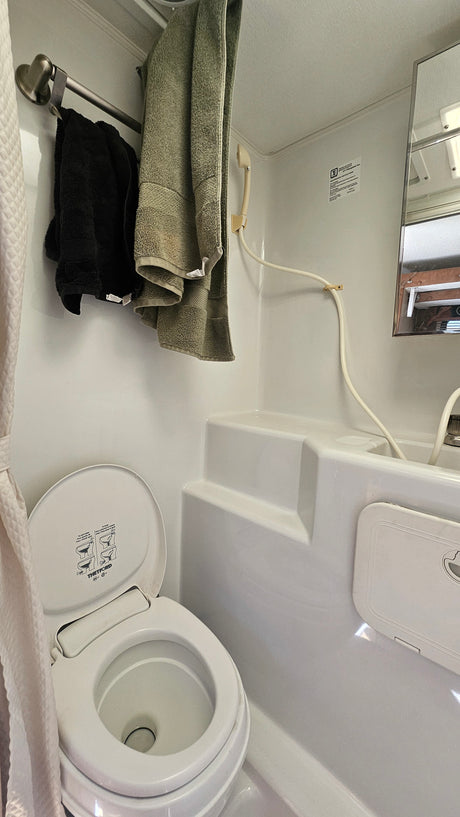 RV rental bathroom with a compact Thetford toilet, handheld shower, towel rack, and molded white interior. Functional for travel.