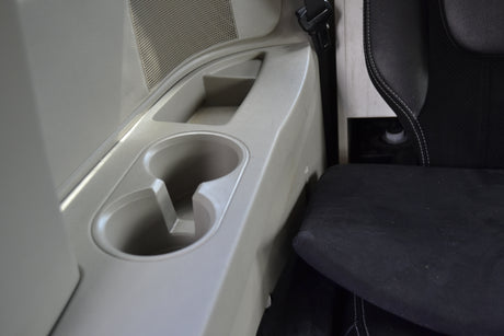 RV rental interior showing a light-colored console with cup holders, storage, and a speaker, next to a black seat.