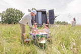Family picnic with an RV rental: a man helps two children at a table in a grassy field, a woman stands by the open van.