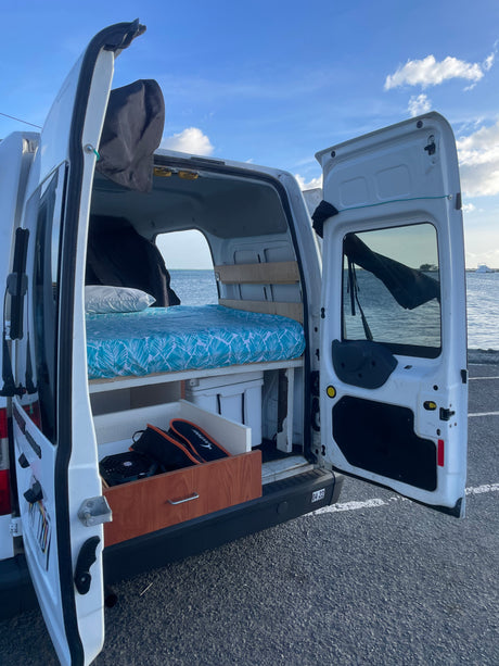 Inside an rv rental, a converted camper van features a comfy bed and storage, parked seaside for scenic travel.