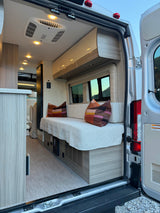 Inside a modern rv rental camper van, seen from open rear doors. Features a comfy bench, storage, AC, and bright interior.
