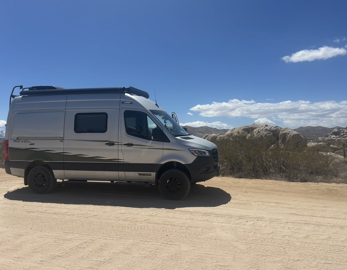 Silver Winnebago Revel 4x4 camper van parked on a dirt road in a sunny desert landscape. Perfect for your next RV rental adventure.