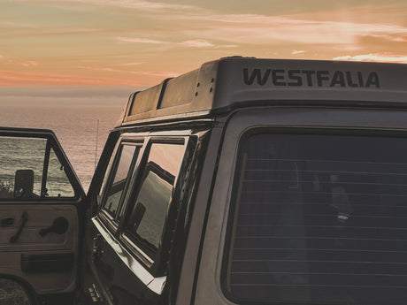 Serene sunset view from a classic Westfalia camper van by the ocean. Envision your next RV rental road trip!