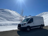 A white Ford Transit van, ideal for your next rv rental adventure, parked on a sunny day in snowy mountains with ski tracks.