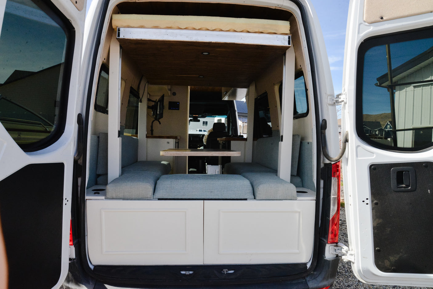Rear view of a modern camper van interior, showcasing a dinette, table, and overhead bed. Perfect for an RV rental getaway!