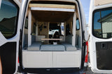 Rear view of a modern camper van interior, showcasing a dinette, table, and overhead bed. Perfect for an RV rental getaway!