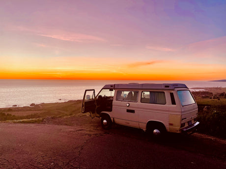 Camper van parked at sunset by the ocean. Ideal RV rental for coastal adventures & van life.