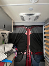 RV rental interior: Overhead AC unit, storage, stacked bedding, and fabric screens covering the red rear doors.