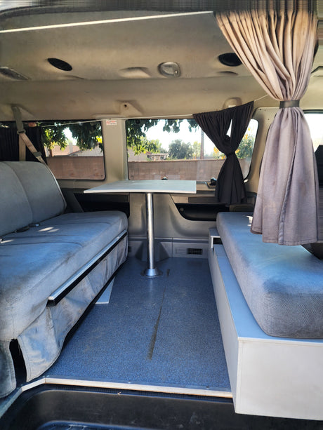 Cozy rv rental interior with facing benches, central table, and curtains, ideal for compact travel and camping.