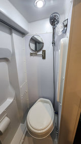 This compact RV rental wet bath features a toilet, handheld shower, and magnifying mirror, optimized for small spaces.