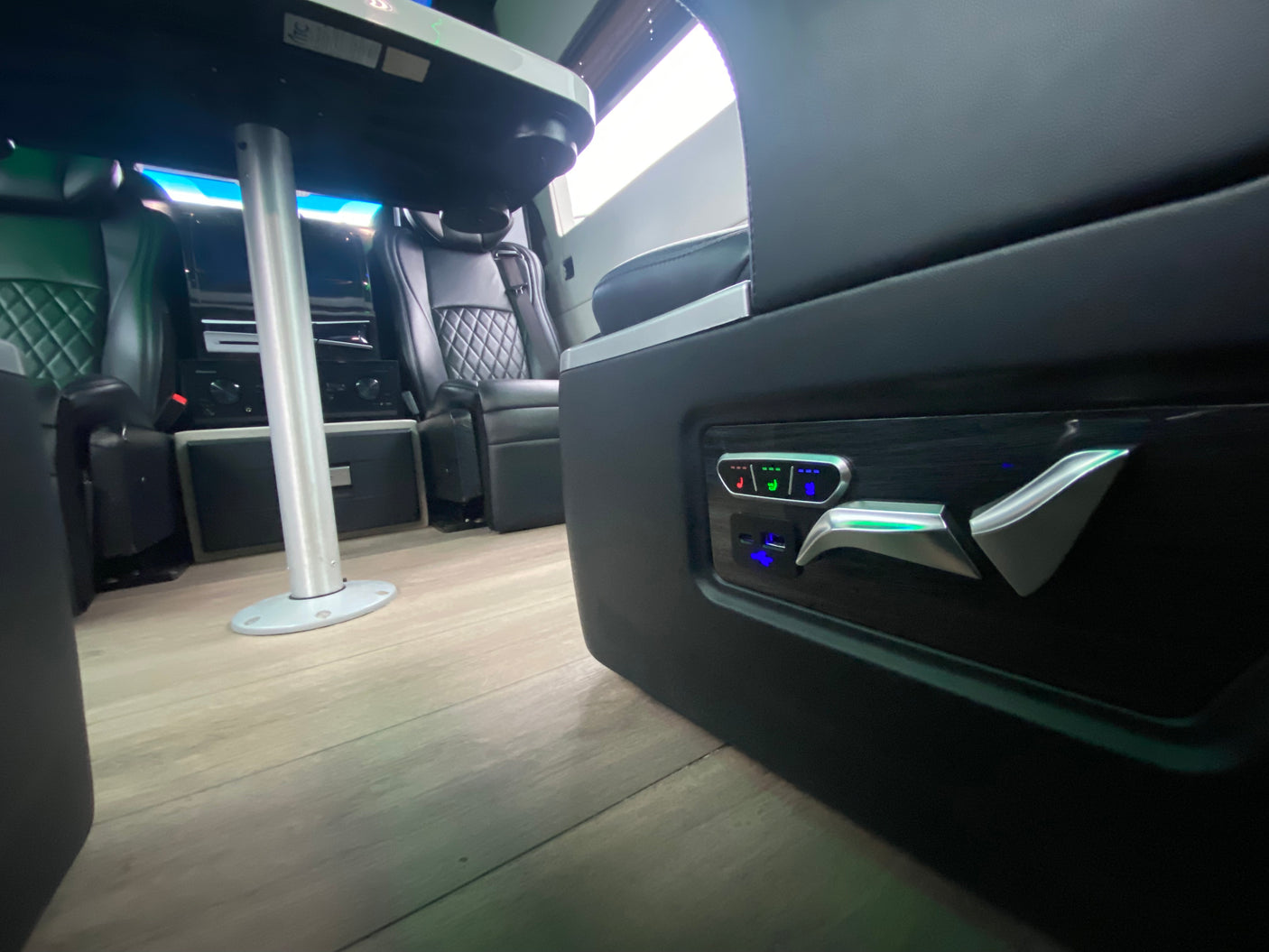 Luxury RV rental interior with illuminated seat controls, quilted seating, and a dining table.