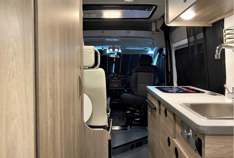 Experience adventure with this spacious rv rental. View of camper van interior showing kitchen, swivel seating, and cockpit.