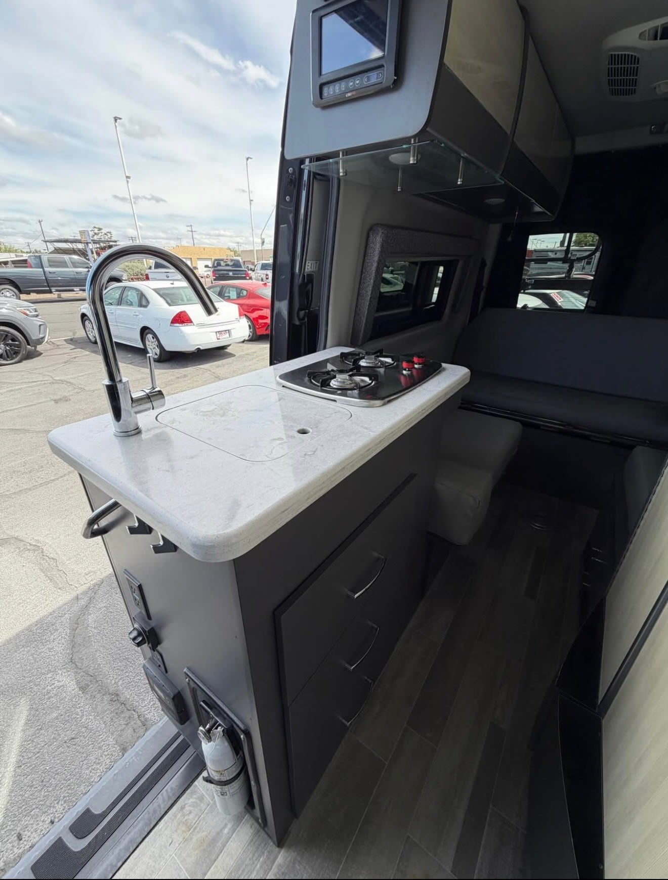This RV rental shows a compact interior with a full kitchen: sink, 2-burner stove, dark cabinets, & control panel. Perfect for adventures.