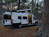 Experience nature with this Winnebago Solis rv rental parked in a forest. Doors open, pop-top up, ready for adventure.