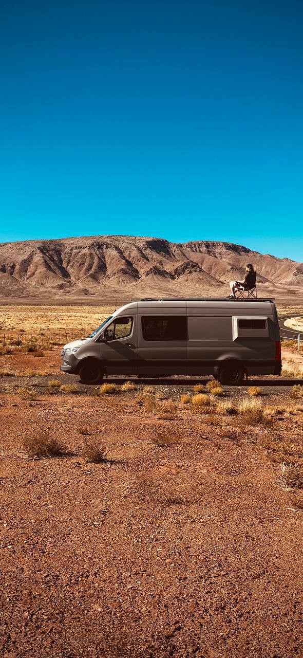  surrounded by vast desert and rugged mountains under a clear blue sky.|Person in a fur hat squats on an RV rental Mercedes Sprinter in a snowy — photo 2