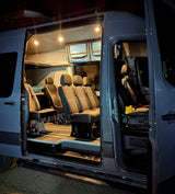 Brightly lit, customized van interior for rv rental, showing passenger seating, overhead storage, and rugged flooring, ideal for group adventures.