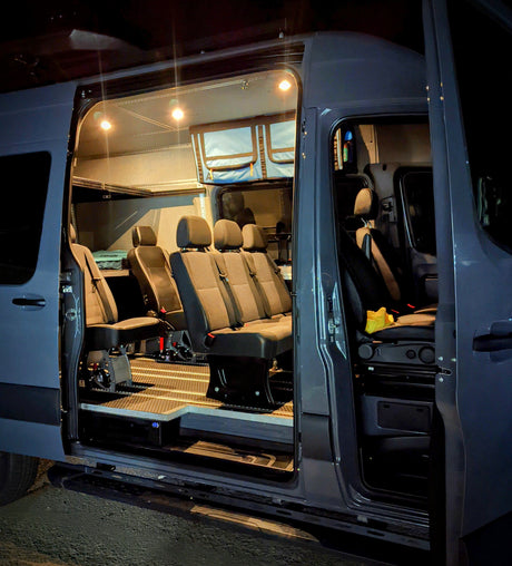 Brightly lit, customized van interior for rv rental, showing passenger seating, overhead storage, and rugged flooring, ideal for group adventures.