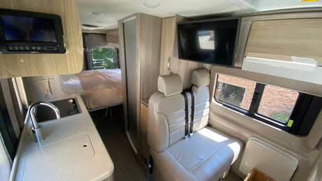 Inside this RV rental: view of the kitchen counter with sink, bed area, comfy seating, and wall-mounted TV.