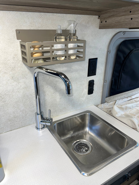 Clean RV rental kitchen with a stainless steel sink, chrome faucet, and lavender cedarwood products on a wall-mounted shelf.